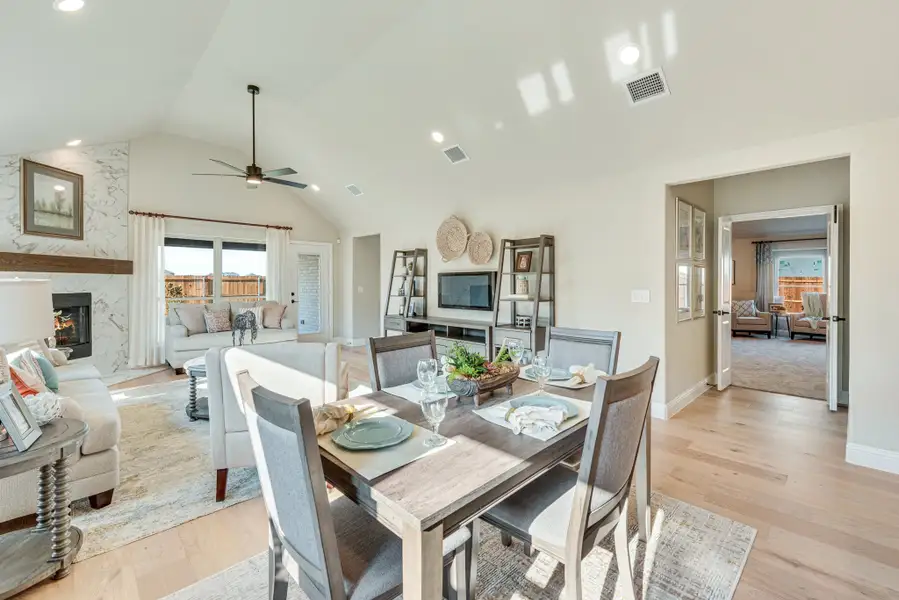 Open-concept dining and living area with vaulted ceiling, wood floors, and stone fireplace