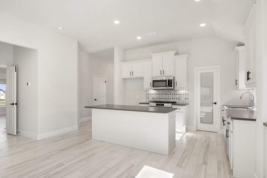 Open kitchen with white cabinets, center island, dark countertops, and stainless steel appliances on light wood floors