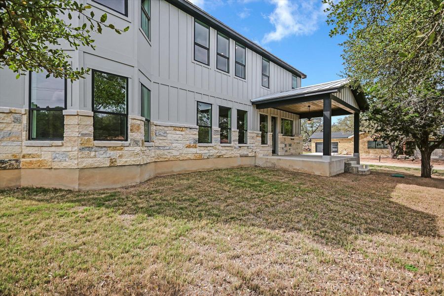 Back of house with board and batten siding, a patio, a lawn, and stone siding