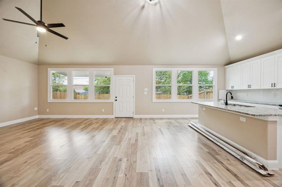 Kitchen featuring white cabinets, high vaulted ceiling, light wood-style floors, tasteful backsplash, and light stone countertops Kitchen featuring white cabinets, high vaulted ceiling, light wood-style floors, tasteful backsplash, and light stone countertops