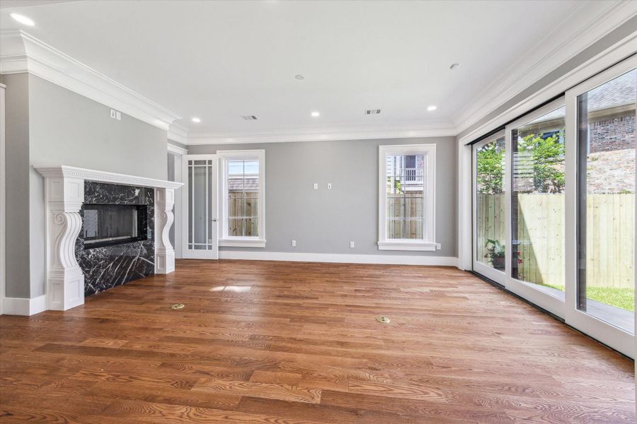 This highlights the spacious den/family room that  features elegant hardwood floors, a striking black marble surround fireplace, and large sliding glass doors that provide plenty of natural light and open to the covered patio and fenced backyard. The soft gray walls and crown molding add a touch of sophistication.