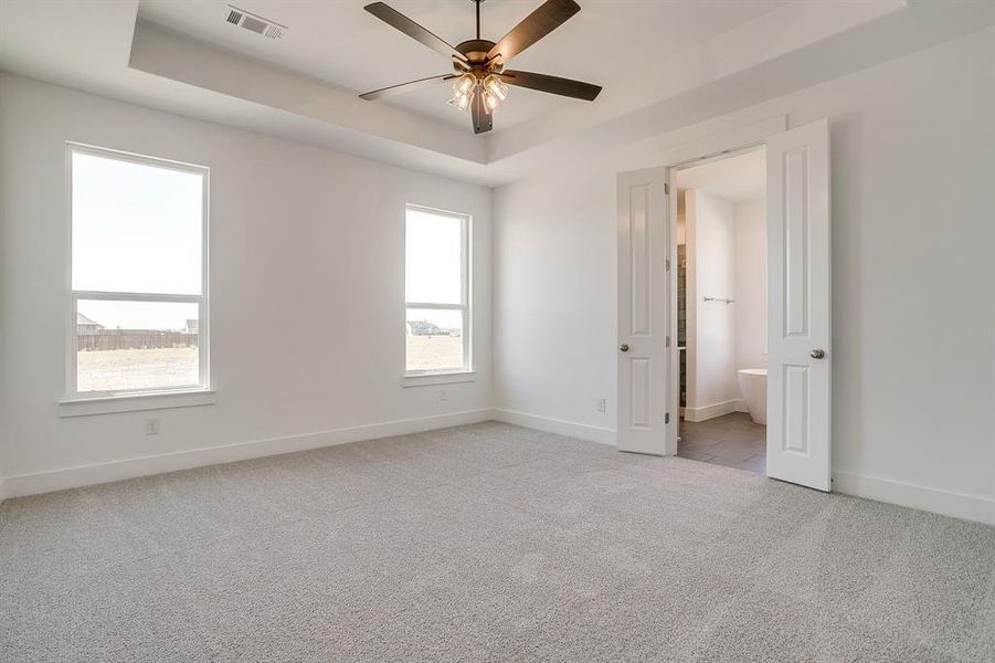 Unfurnished bedroom with a raised ceiling, light carpet, and a ceiling fan Unfurnished bedroom with a raised ceiling, light carpet, and a ceiling fan