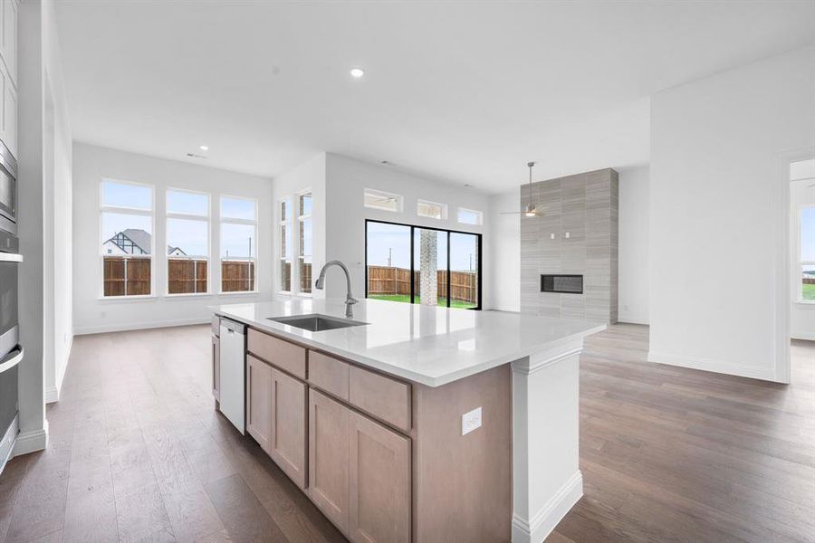 Kitchen with light brown cabinetry, dishwasher, sink, dark hardwood / wood-style flooring, and a kitchen island with sink