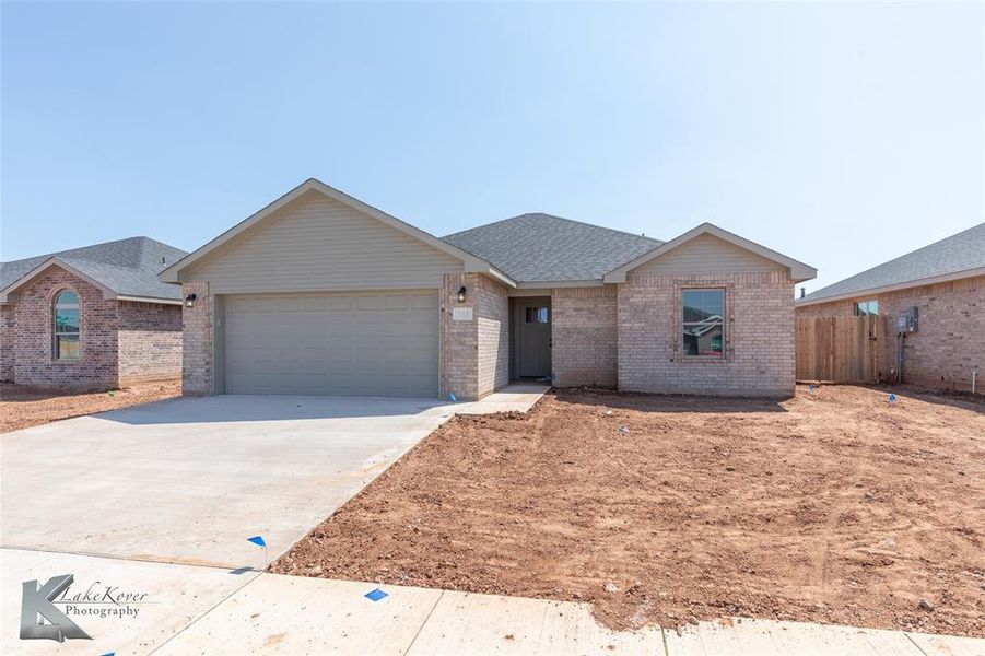 Single story home featuring concrete driveway, brick siding, roof with shingles, and an attached garage