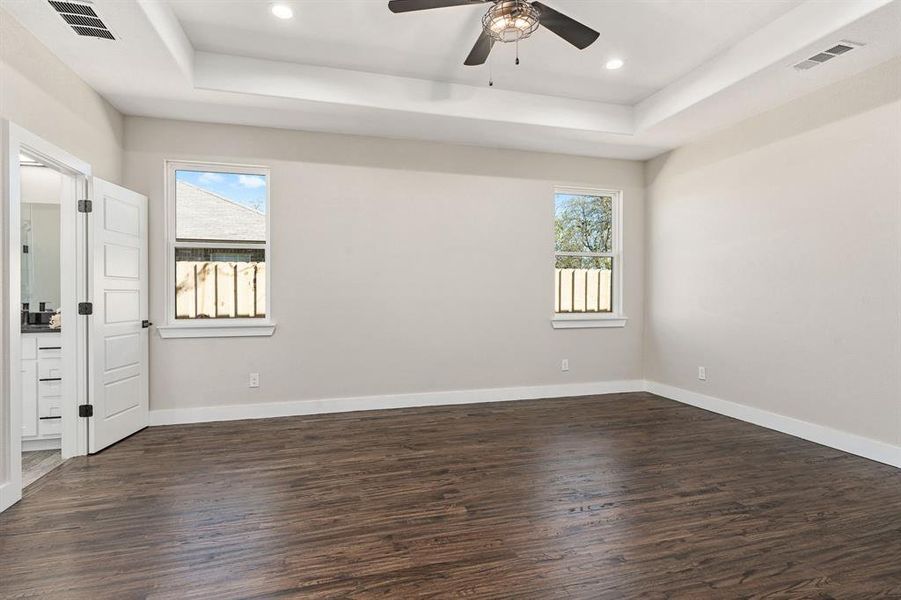 Spare room with a tray ceiling, dark wood-type flooring, ceiling fan, and plenty of natural light