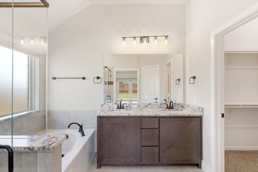 Master bathroom with double vanity, granite countertops, soaking tub, and walk-in closet entrance