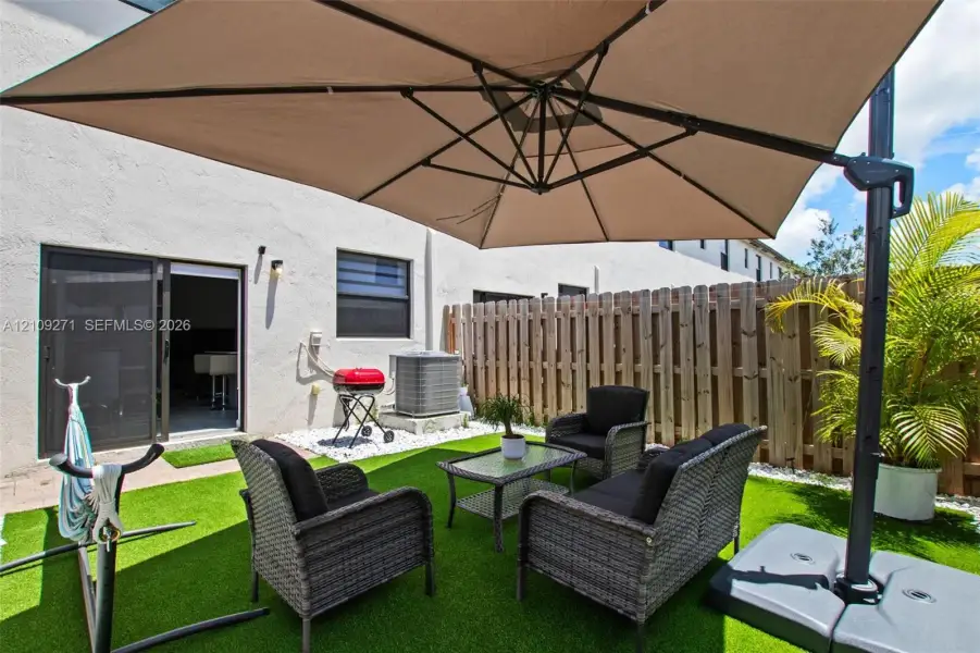 Rear patio featuring synthetic turf, perimeter wood privacy fencing, and sliding glass door access