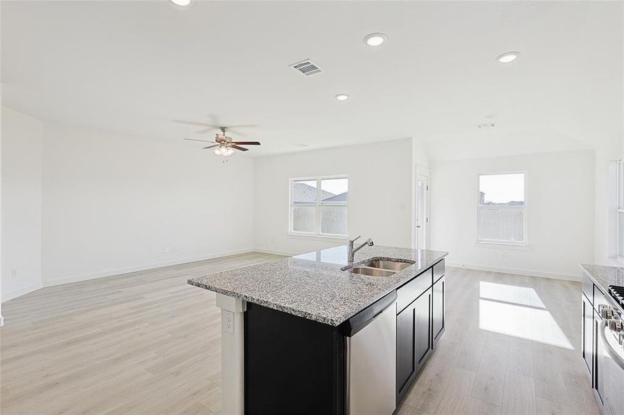 Kitchen featuring light wood-type flooring, ceiling fan, sink, dishwasher, and an island with sink