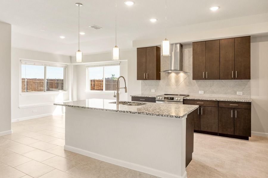 Kitchen with large granite island, dark brown cabinets, stainless steel range hood, and pendant lights over tile floors