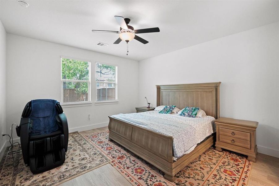 Spacious room featuring light wood-finish flooring, a ceiling fan with integrated lighting, and two large windows providing natural light Spacious room featuring light wood-finish flooring, a ceiling fan with integrated lighting, and two large windows providing natural light