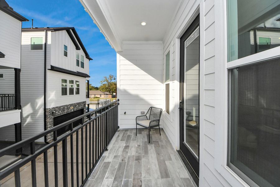 This photo shows a modern balcony with stylish wood-look tile flooring and a black metal railing. It features a sliding glass door and offers a view of neighboring homes with a similar contemporary design. The space includes a chair, ideal for relaxing outdoors. This photo shows a modern balcony with stylish wood-look tile flooring and a black metal railing. It features a sliding glass door and offers a view of neighboring homes with a similar contemporary design. The space includes a chair, ideal for relaxing outdoors.