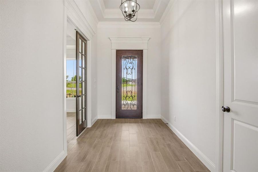 Foyer entrance with wood tiled floors, hanging lights, and a raised ceiling