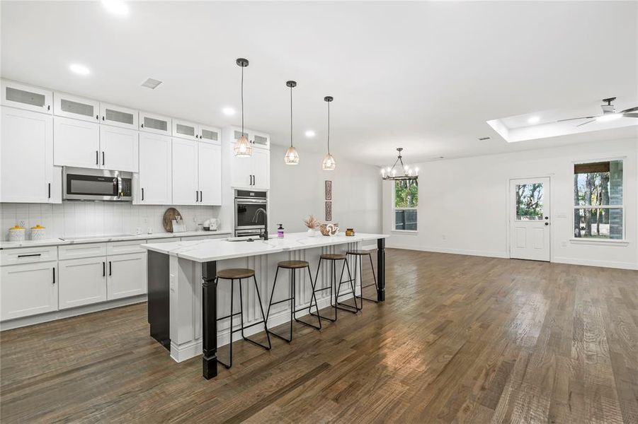 Kitchen featuring a kitchen breakfast bar, white cabinetry, a center island with sink, open floor plan, and pendant lighting