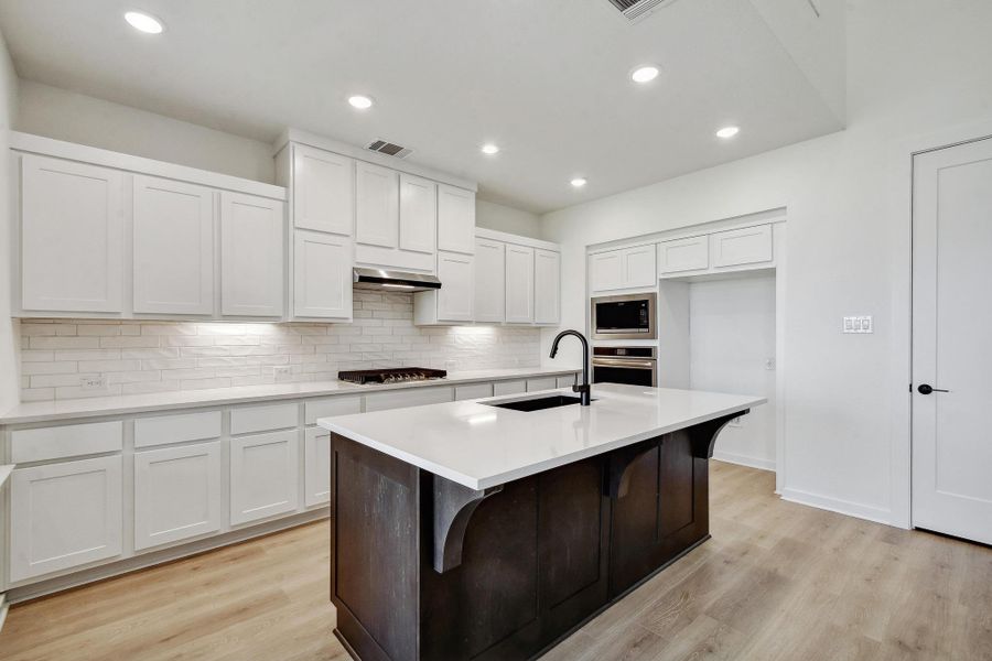 Kitchen with stainless steel appliances, tasteful backsplash, white cabinets, light wood-style flooring, and light countertops