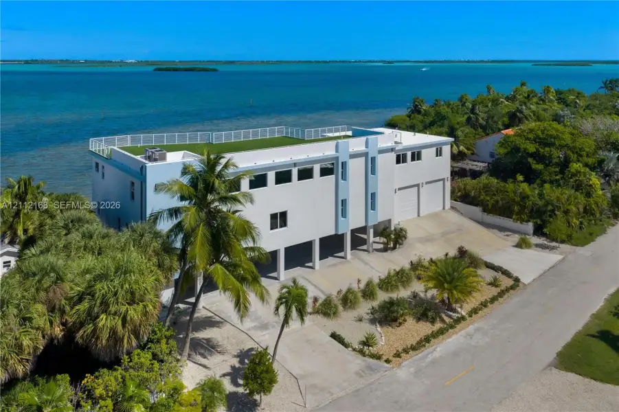 Waterfront residence featuring a rooftop terrace, elevated construction, concrete driveway, and attached two-car garage Waterfront residence featuring a rooftop terrace, elevated construction, concrete driveway, and attached two-car garage