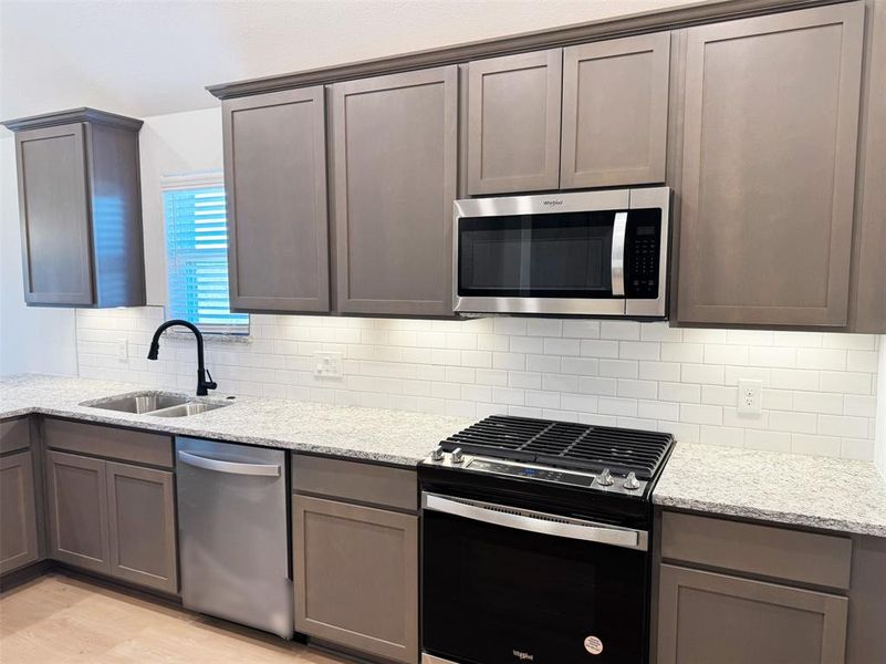 Kitchen with light stone counters, backsplash, a sink, light wood-type flooring, and appliances with stainless steel finishes