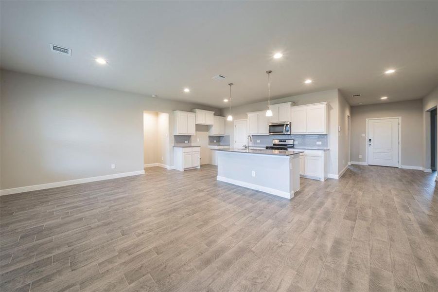 Kitchen with white cabinets, decorative light fixtures, light wood-type flooring, appliances with stainless steel finishes, and an island with sink