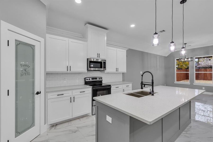 Kitchen with appliances with stainless steel finishes, sink, decorative light fixtures, white cabinetry, and an island with sink