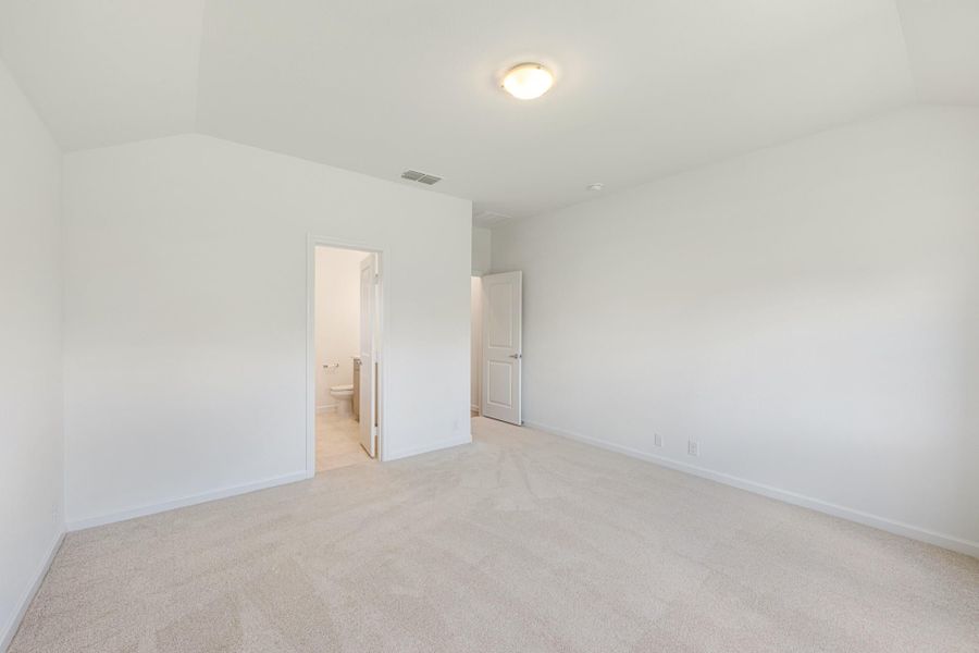 Empty bedroom with beige carpet, white walls, ensuite bathroom doorway, and closet door Empty bedroom with beige carpet, white walls, ensuite bathroom doorway, and closet door