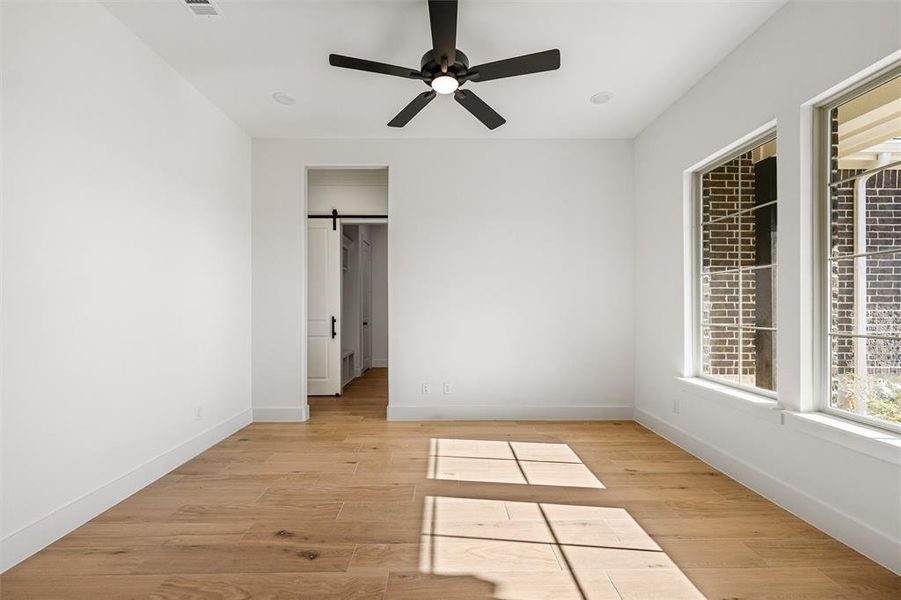 Unfurnished bedroom featuring a barn door, light wood finished floors, and ceiling fan