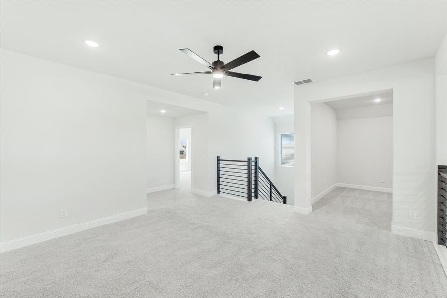 Open upstairs loft with carpet, ceiling fan, and black metal stair railing along open staircase