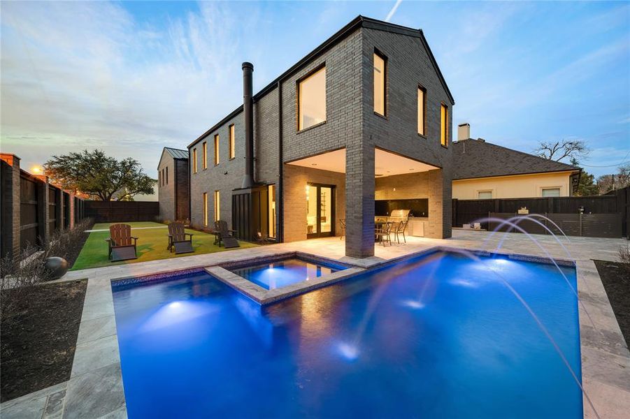 Pool at dusk with a patio area, a fenced backyard, a lawn, and a pool with connected hot tub