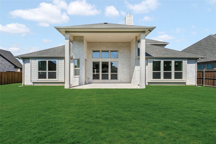 Rear exterior of single-story brick home with covered patio and large fenced backyard