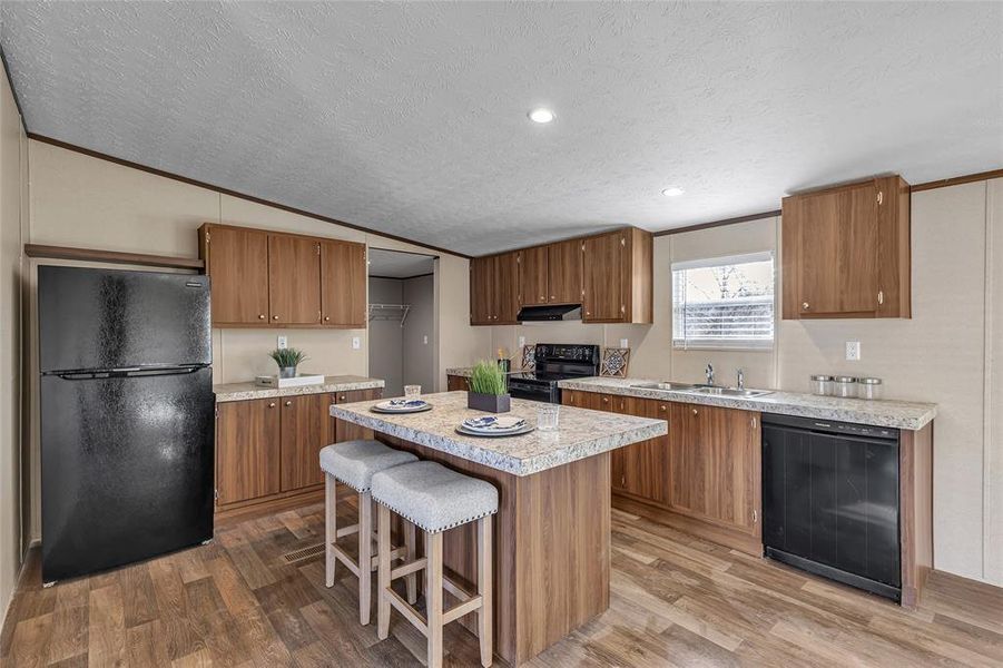 Kitchen with vaulted ceiling, light hardwood / wood-style flooring, a center island, black appliances, and sink