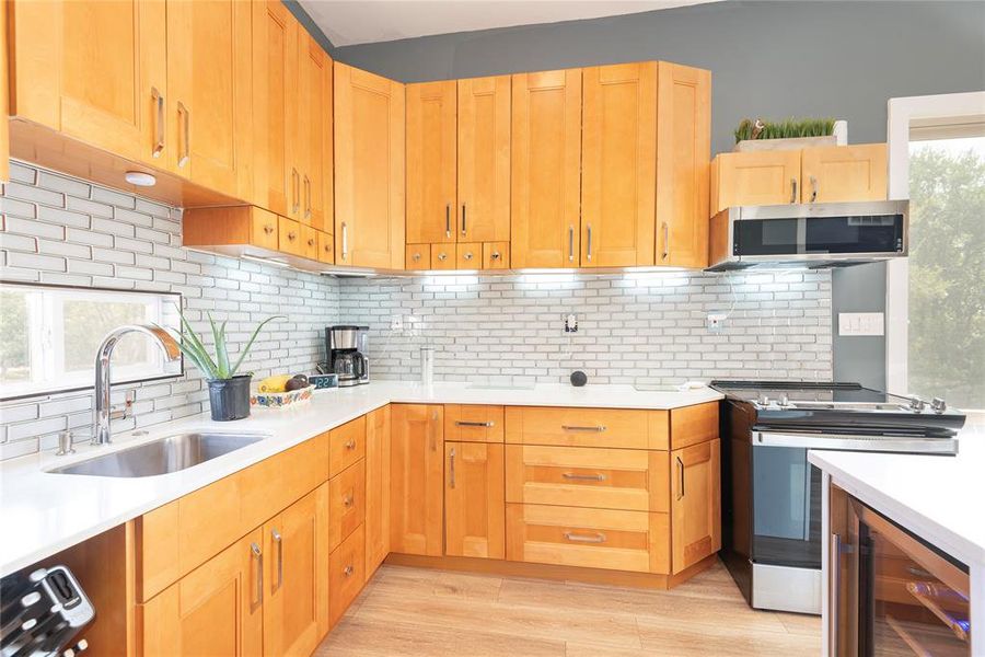 Kitchen with tasteful backsplash, stainless steel appliances, wine cooler, light wood-style floors, and light stone countertops Kitchen with tasteful backsplash, stainless steel appliances, wine cooler, light wood-style floors, and light stone countertops