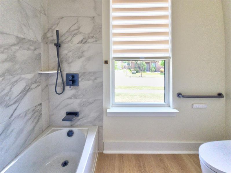 Bathtub with marble-style tile surround, matte black fixtures, and a wall-mounted grab bar