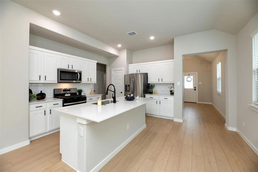 Kitchen featuring decorative backsplash, white cabinets, appliances with stainless steel finishes, vaulted ceiling, and an island with sink Kitchen featuring decorative backsplash, white cabinets, appliances with stainless steel finishes, vaulted ceiling, and an island with sink