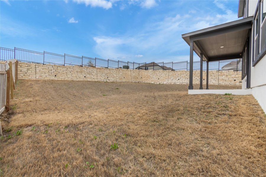 A spacious backyard with a covered patio offers outdoor living space and a retaining wall with fencing.