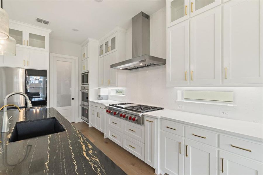 Kitchen with wall chimney range hood, white cabinets, wood finished floors, and stainless steel appliances