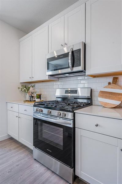 Kitchen with stainless steel appliances, light hardwood / wood-style flooring, tasteful backsplash, and white cabinets