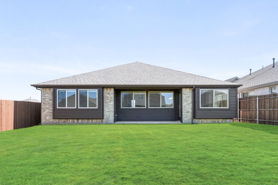Single-story home rear exterior with brick and dark siding, large windows, and fenced backyard with green lawn