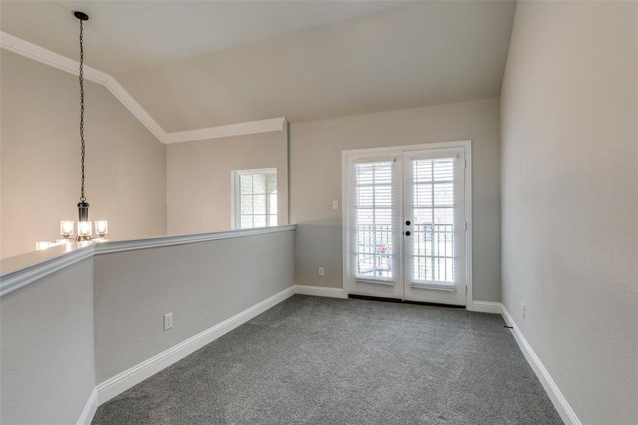 Loft space featuring crown molding, french doors to balcony, lofted ceiling, an inviting chandelier, and carpet