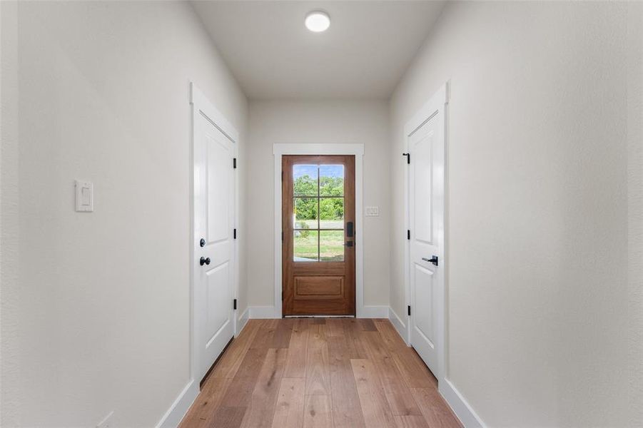 Entryway featuring wood-finish flooring, a wood-paneled door with glass inserts, and two white panel doors with matte black hardware
