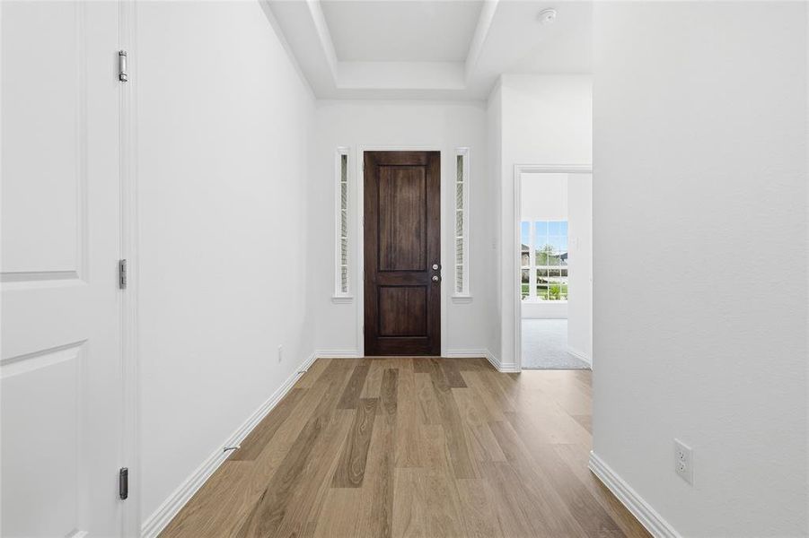 Entryway featuring wood-finish flooring, a dark wood-paneled door with sidelight windows, and a tray ceiling