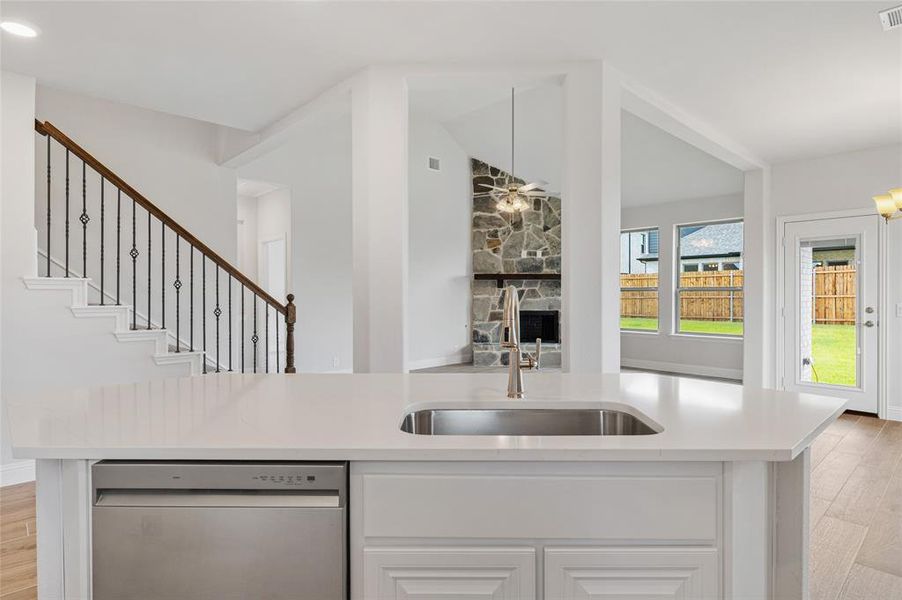 Kitchen featuring light wood finished floors, stainless steel dishwasher, white cabinetry, a center island with sink, and vaulted ceiling