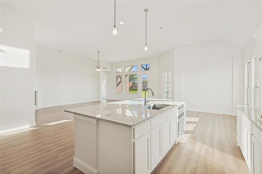 Kitchen featuring an island with sink, light hardwood / wood-style flooring, sink, decorative light fixtures, and white cabinets