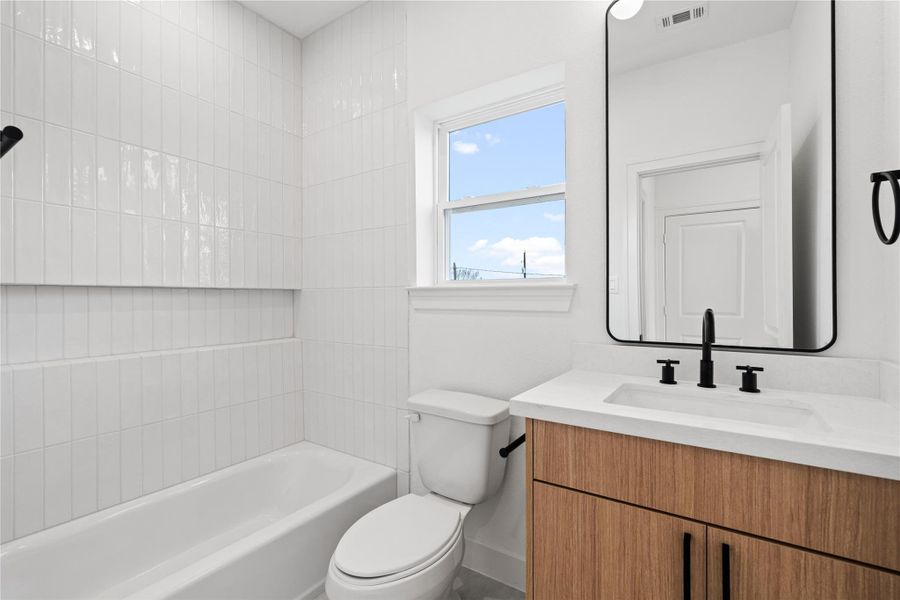 Secondary bathroom with a bright window, modern finishes, and a clean tiled tub surround.