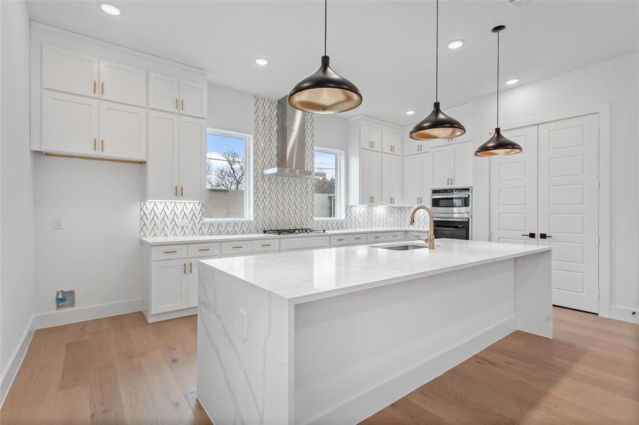 Kitchen featuring decorative backsplash, light wood-type flooring, wall chimney exhaust hood, and an island with sink