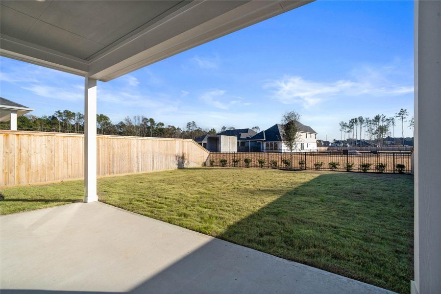 Step outside to a private backyard oasis, perfect for relaxing or outdoor entertaining. The yard offers a blend of privacy with a tall wood fence and an open feel provided by a black metal fence, overlooking the surrounding community and mature trees.