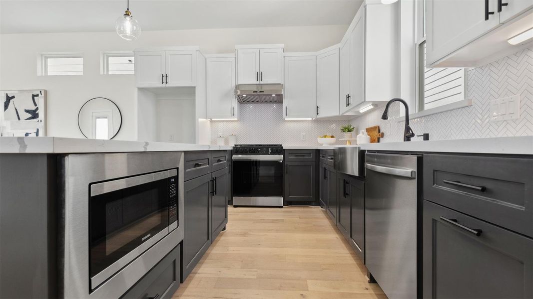 Modern kitchen featuring white countertops, custom dark cabinetry, stainless steel appliances, a central island, and engineered hardwood floors. This is an upgraded kitchen .