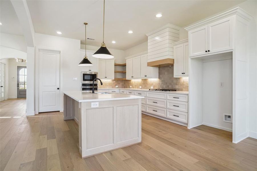 Kitchen featuring a kitchen island with sink, sink, pendant lighting, white cabinets, and light hardwood / wood-style floors