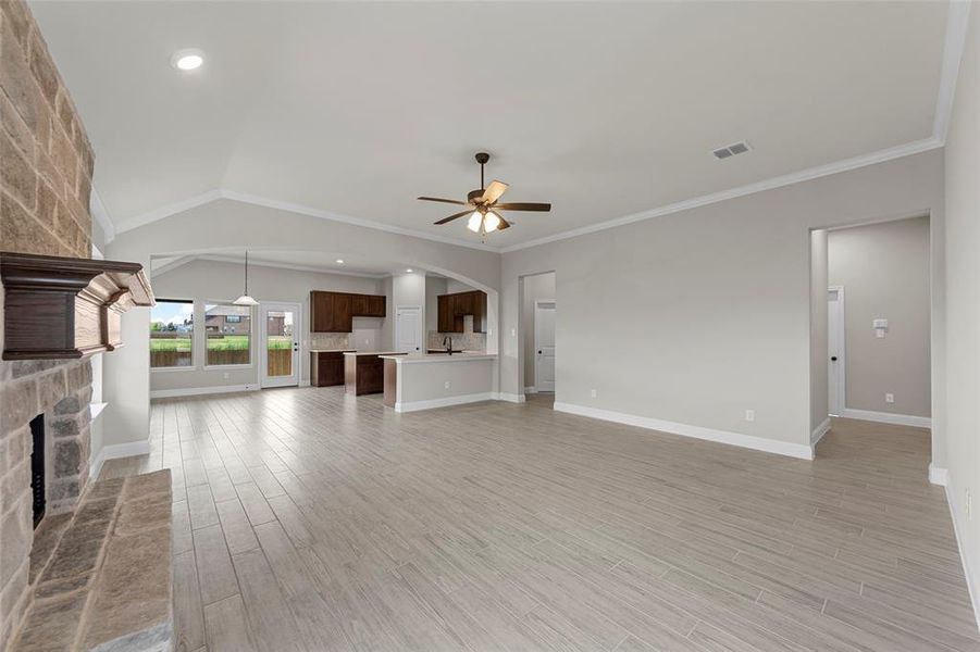 Unfurnished living room featuring light wood-type flooring, a fireplace, ornamental molding, ceiling fan, and vaulted ceiling