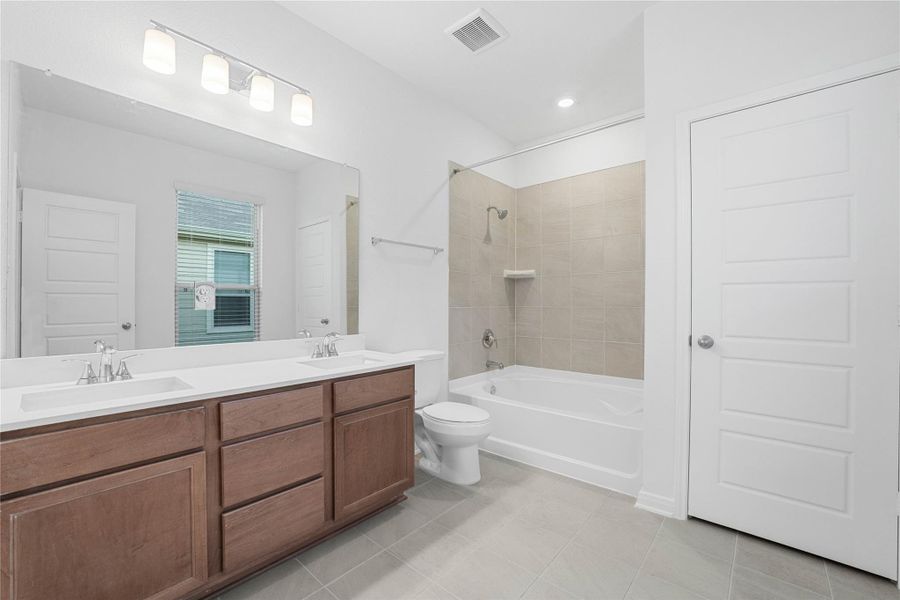 This beautifully updated primary bathroom is move-in ready! It showcases stained cabinetry paired with light countertops, dual vanity sinks, a large mirror, tub/shoewr combination with tile surround, a linen closet with built-in shelving, high ceilings, custom paint, and stylish modern finishes throughout.