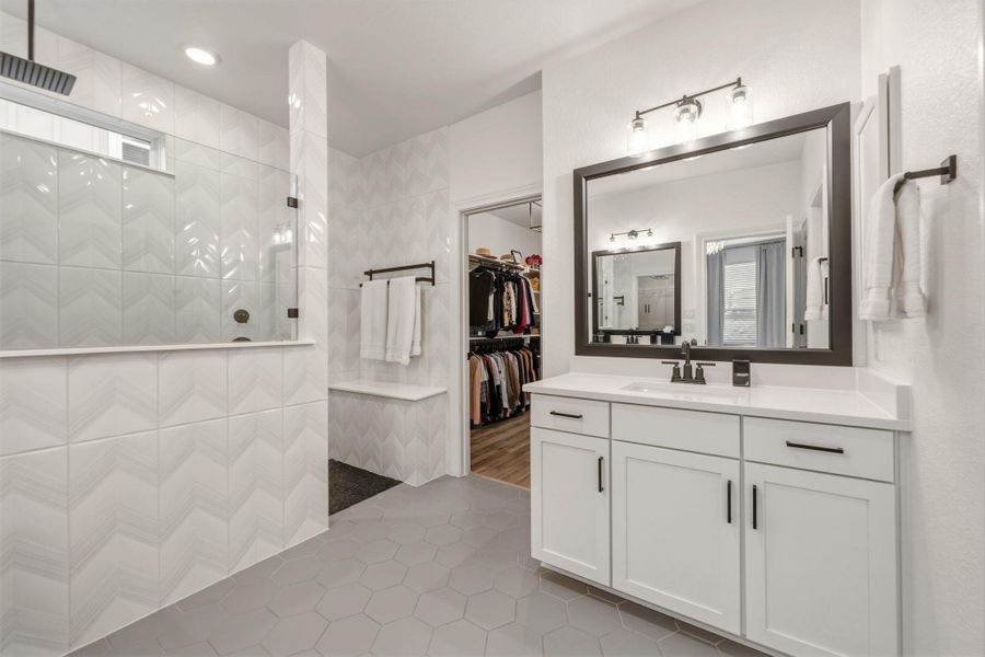 Contemporary bathroom featuring a spacious walk-in shower with decorative tile, hexagon floor tiling, double vanity with a white quartz countertop, and a large framed mirror