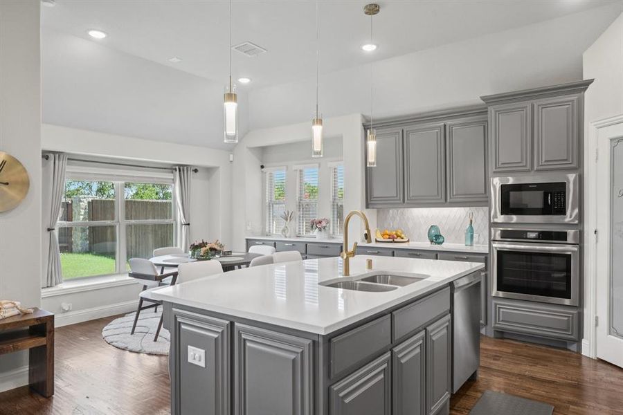 Kitchen featuring stainless steel appliances, gray cabinetry, light countertops, decorative backsplash, and dark wood-type flooring Kitchen featuring stainless steel appliances, gray cabinetry, light countertops, decorative backsplash, and dark wood-type flooring