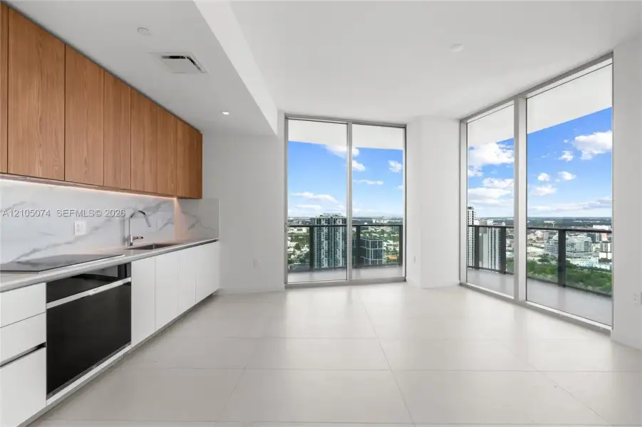Modern kitchen featuring wood-finish upper cabinetry, matte white lower cabinetry, stone-patterned backsplash, integrated appliances, and floor-to-ceiling glass paneling